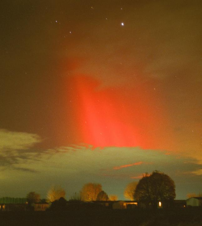 A red aurora is visible in the night sky above a dark landscape with trees and buildings.