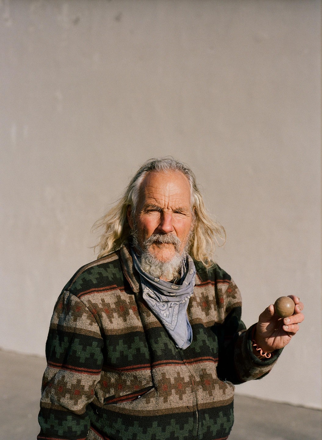 A man with long hair and a beard holds a small ball.