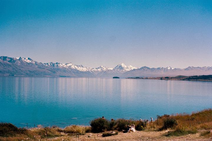 A wide shot shows a lake with snow-capped mountains in the background and a small island in the middle of the lake.