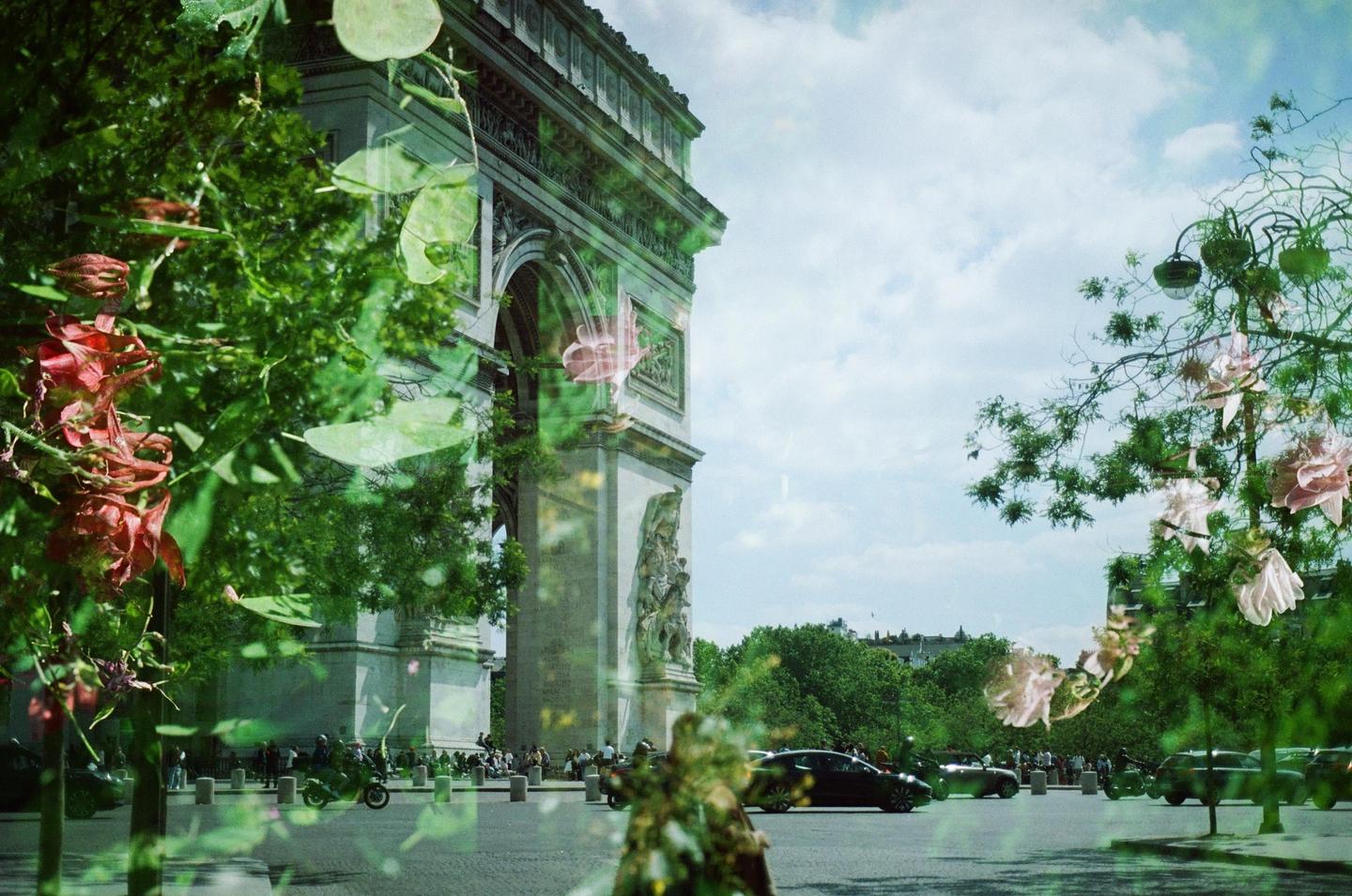 A double exposure shows the Arc de Triomphe and a street with cars and people, overlaid with flowers and foliage.