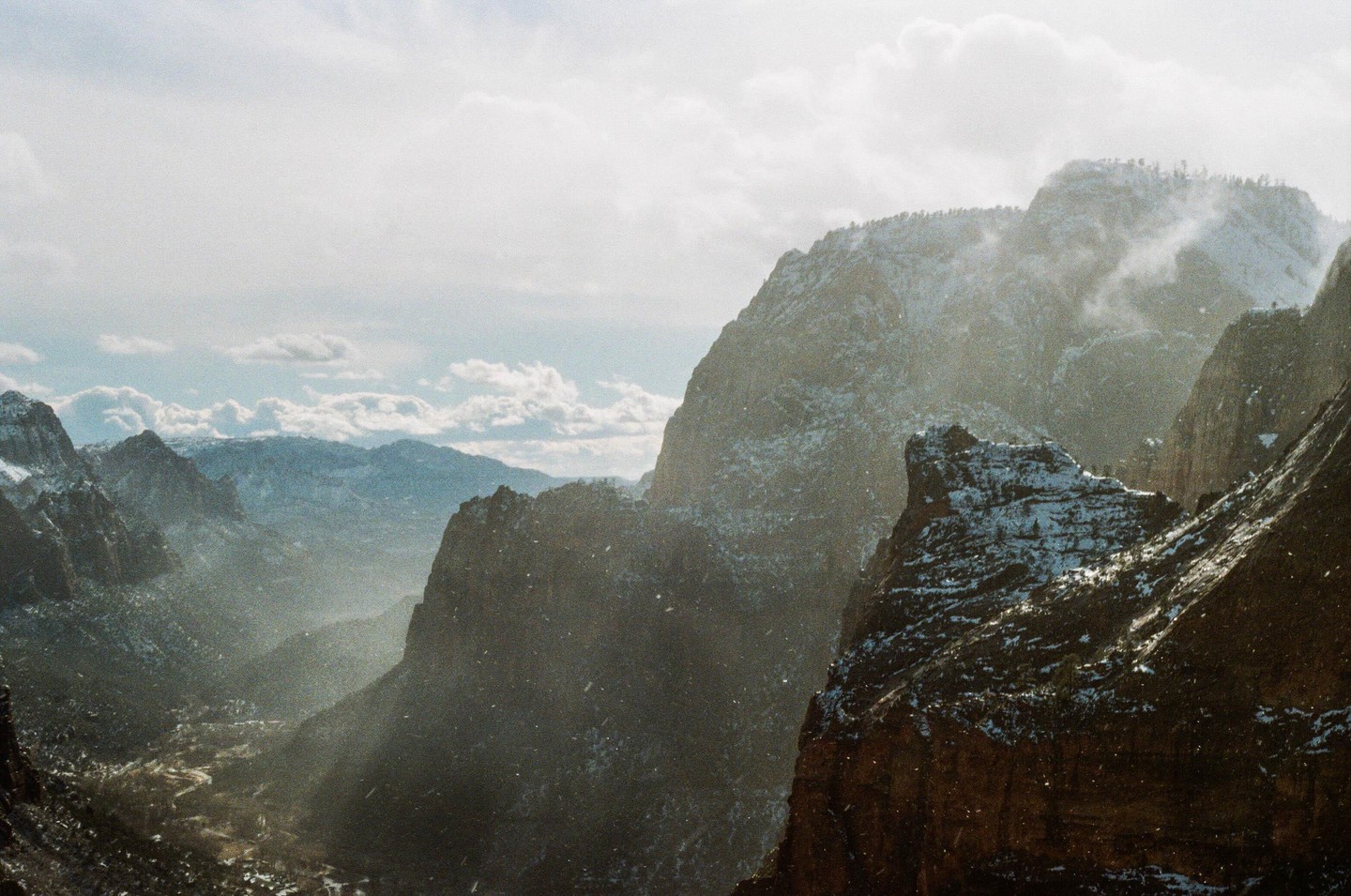 A snowy mountain landscape with clouds and a valley in the distance.