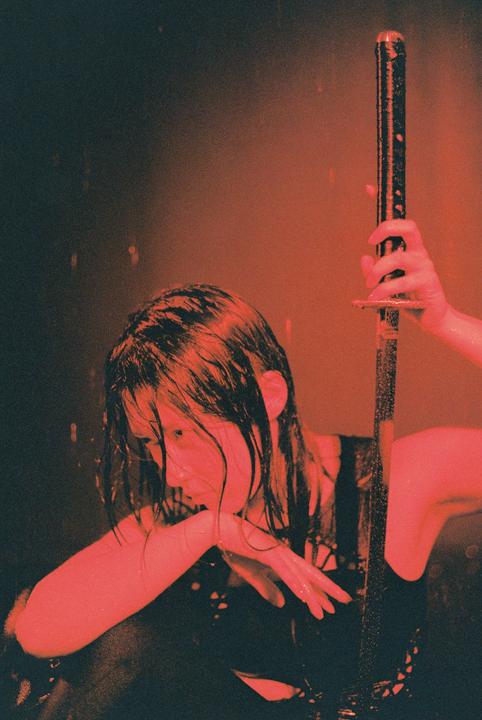 A woman with wet hair holds a katana in a rain studio.
