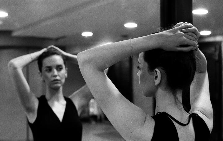 A woman with her hair up looks at her reflection in a mirror.