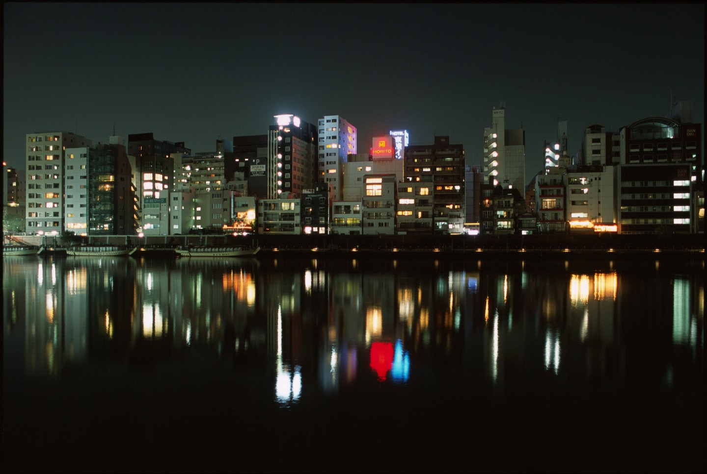 A city skyline with illuminated buildings is reflected in the water at night.