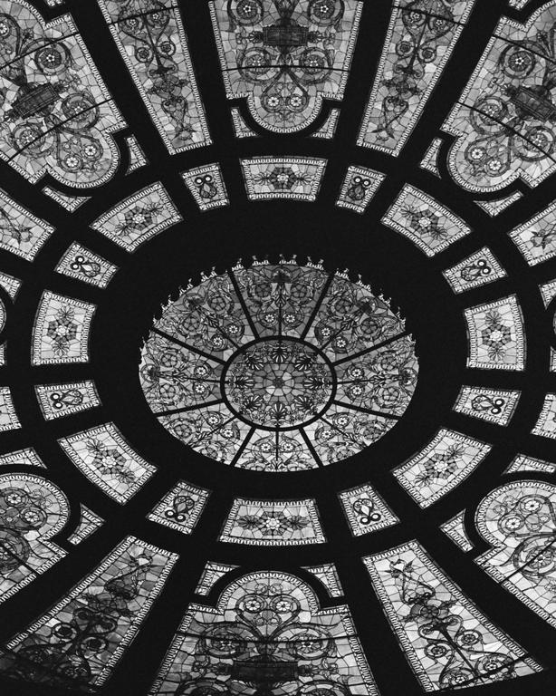 A black and white photograph shows a detailed stained glass ceiling with a circular pattern in the center.