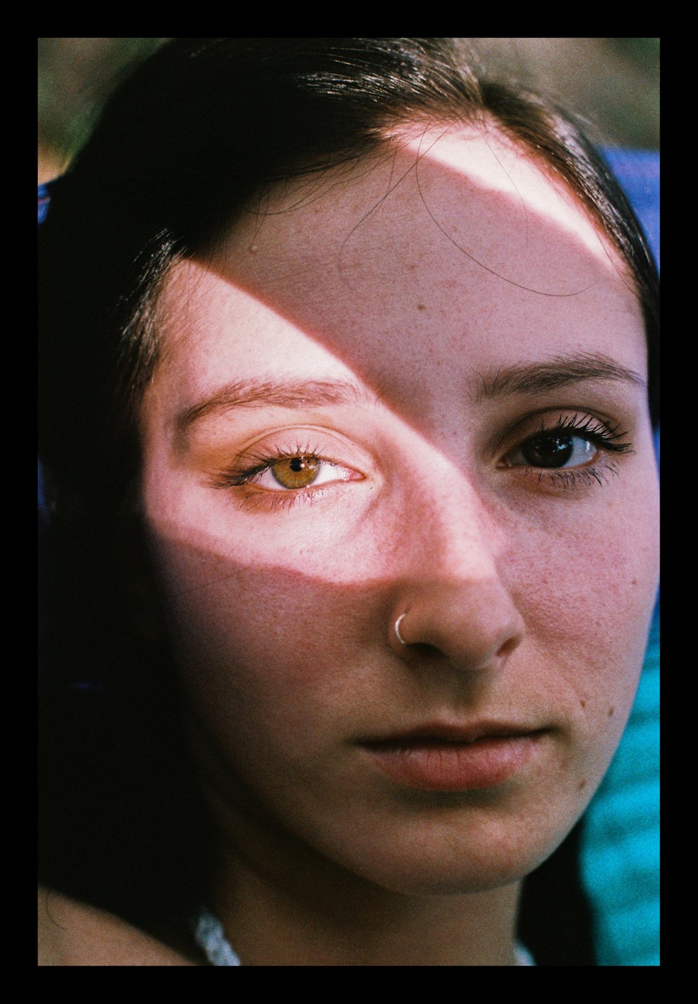 A woman with a nose ring looks directly at the viewer, with a diagonal shadow across her face.