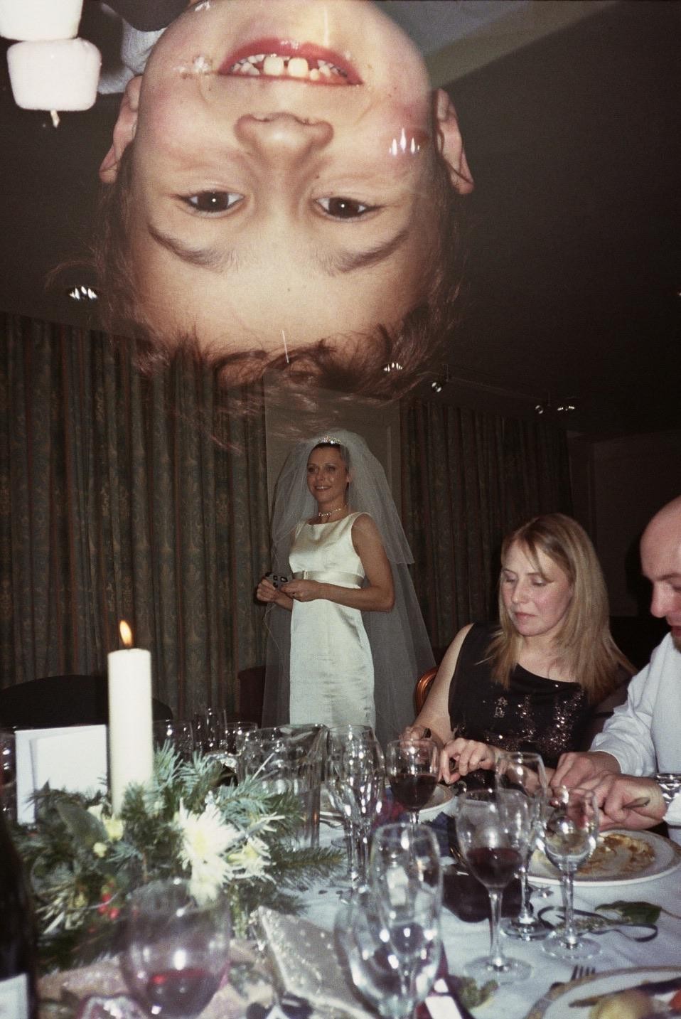 A double exposure shows a child's face upside down above a wedding reception with a bride and guests at a table.