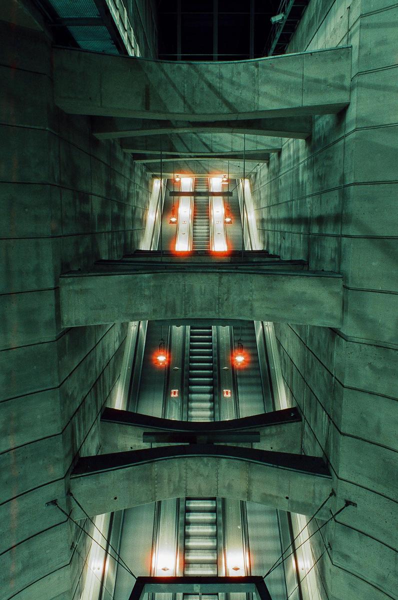 A long exposure shows multiple escalators with glowing red lights in a concrete building.