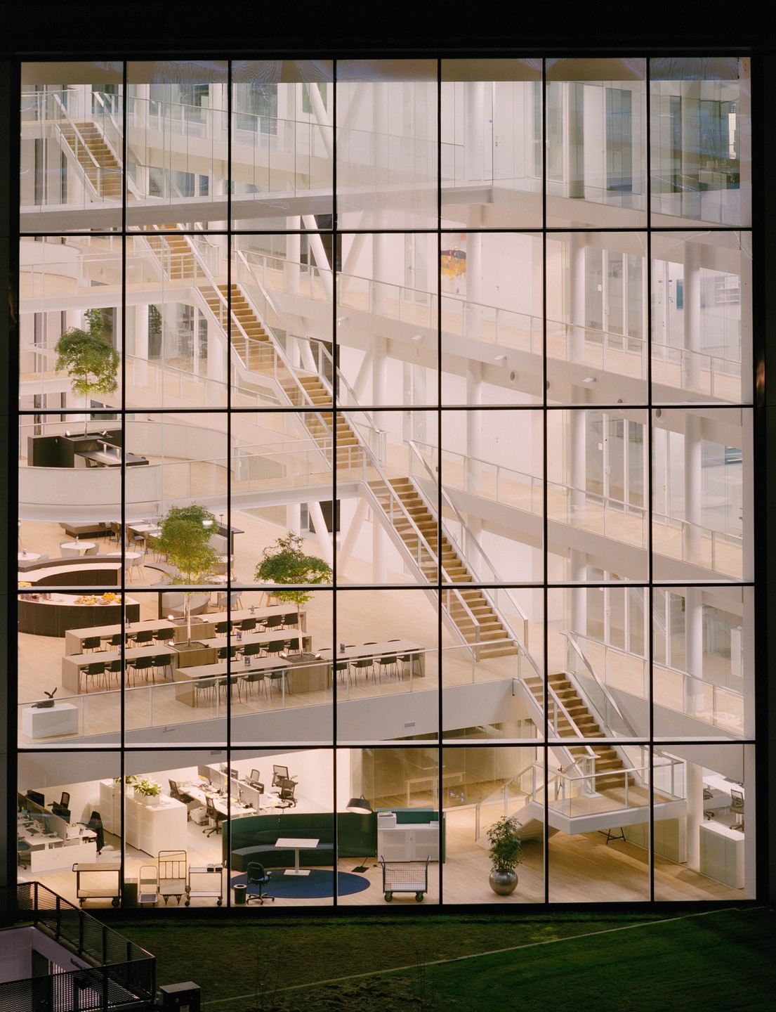 A large, multi-story building with many windows reveals an interior with stairs, tables, and office spaces.