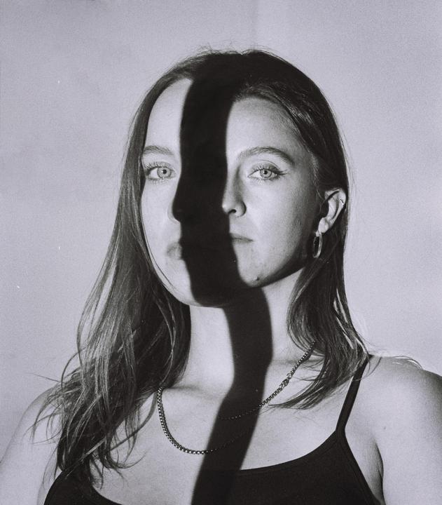 A woman with long hair and a necklace is illuminated by a strong shadow across her face.