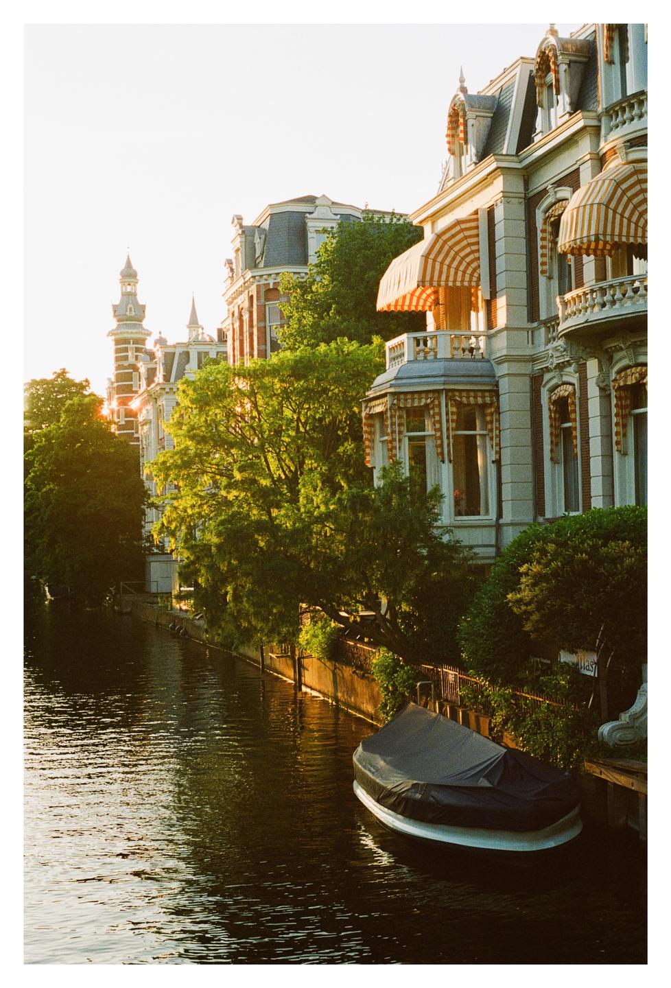 A boat is docked on a canal lined with ornate buildings and trees during golden hour.