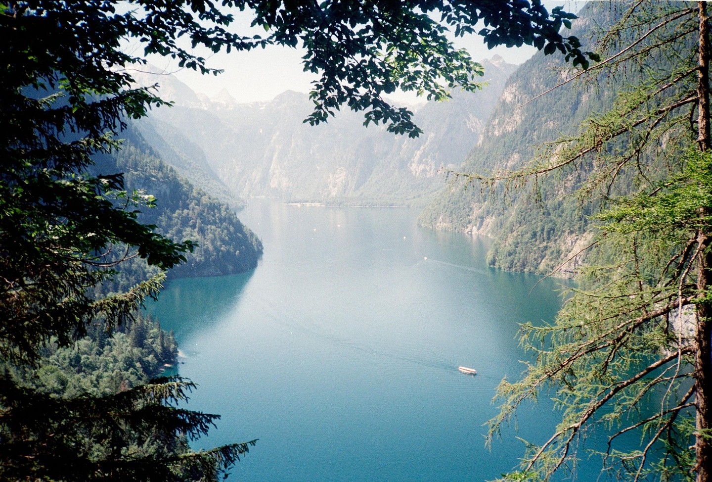 A boat travels across a lake surrounded by mountains and trees.