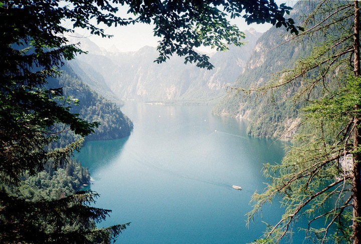 A boat travels across a lake surrounded by mountains and trees.