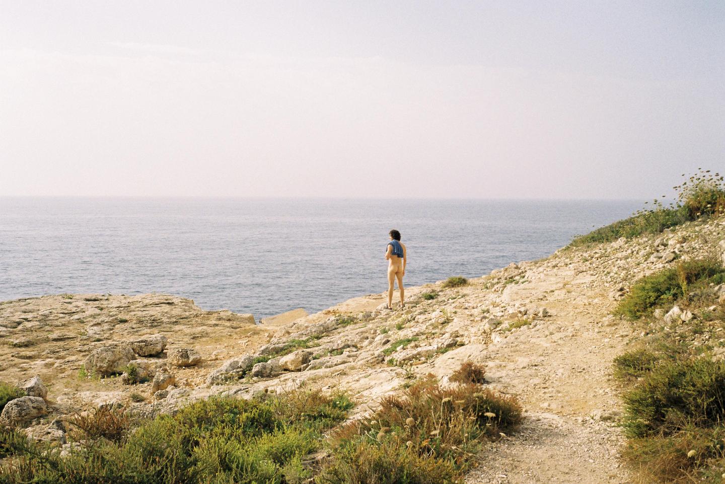 A person stands on a rocky cliff overlooking the ocean.