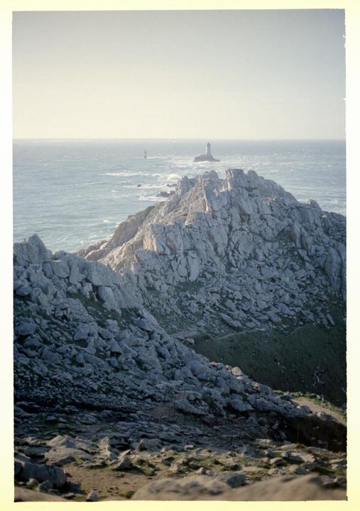 A rocky coastline with two lighthouses in the distance is visible under a bright sky.