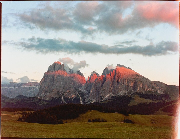 The sun illuminates the peaks of a mountain range with a red glow under a cloudy sky.