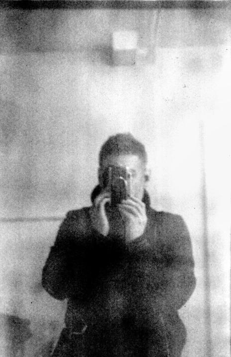 A man takes a self-portrait in a mirror, holding a camera to his face.