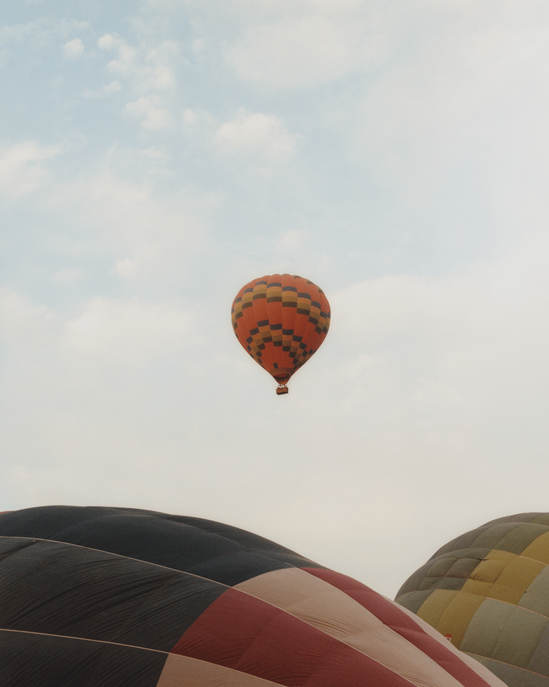 A hot air balloon floats in the sky above other hot air balloons on the ground.