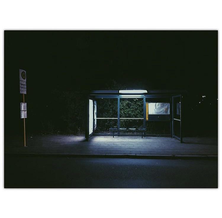 A bus stop with a bench and a sign is illuminated at night.