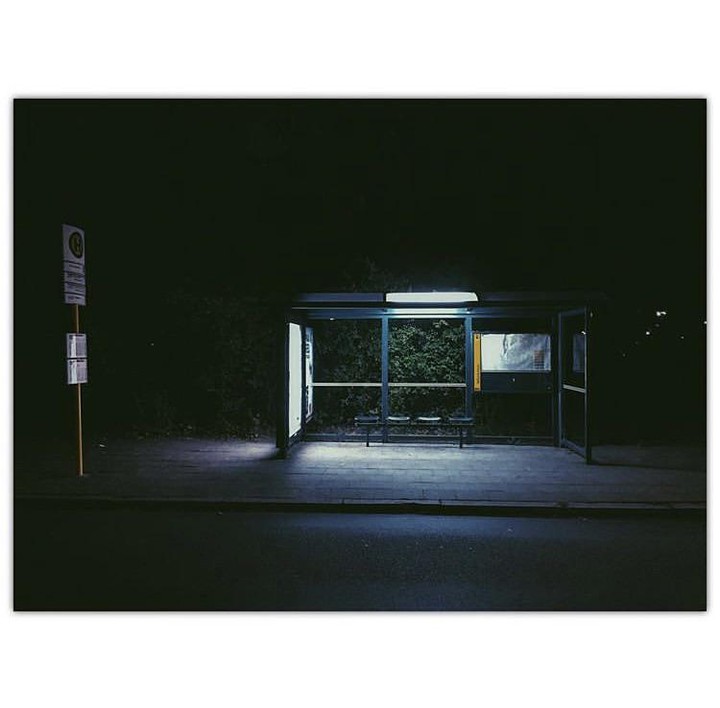 A bus stop with a bench and a sign is illuminated at night.