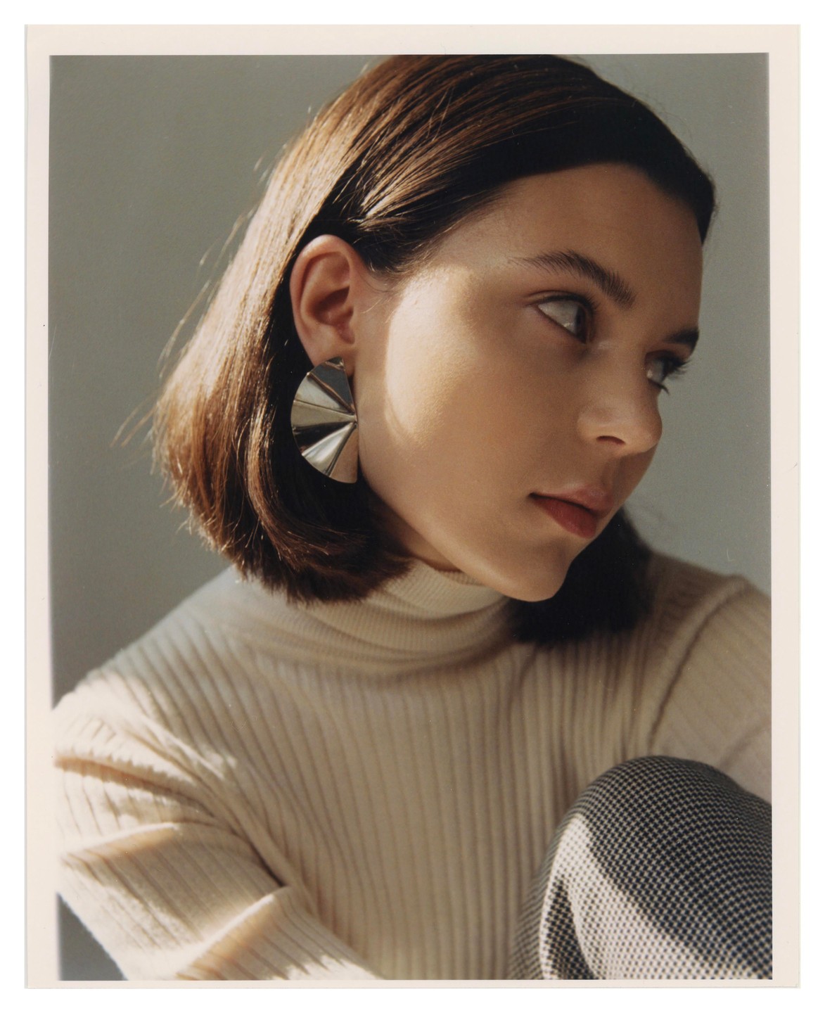 A woman with short brown hair and a cream turtleneck sweater looks to the right.