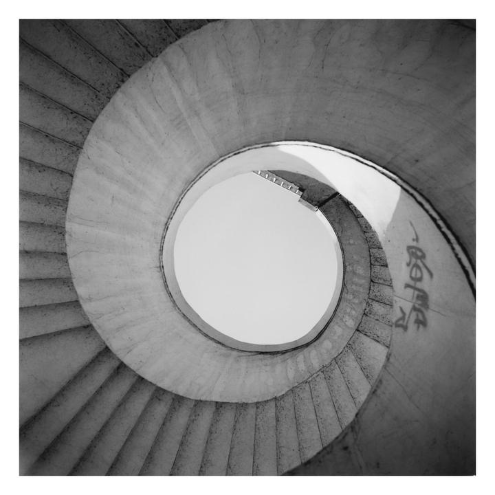 A low-angle view of a spiral staircase shows the steps curving upwards towards a bright circle of sky.