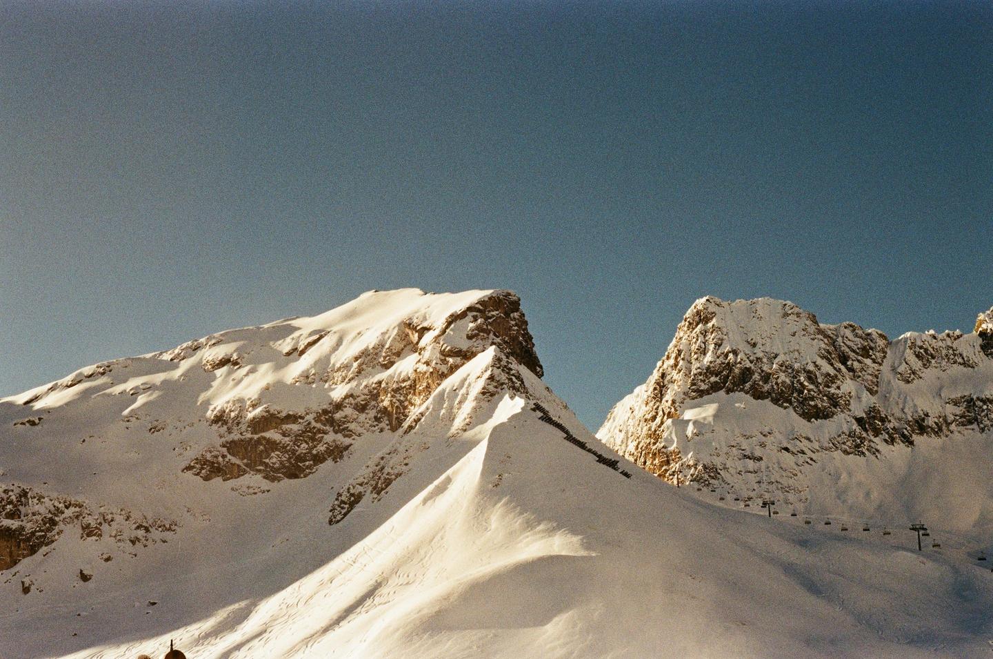 Snow-covered mountains are illuminated by the sun under a clear sky.