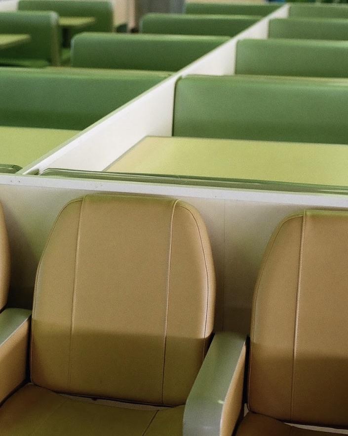 A diner interior shows rows of green booths and tan chairs.