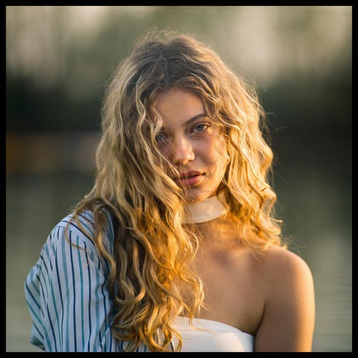 A woman with long, curly hair looks directly at the viewer.