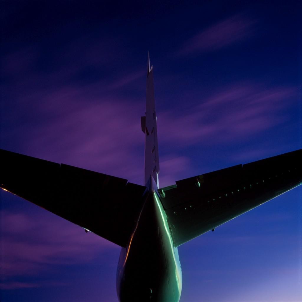 The tail and wing of an airplane are silhouetted against a purple and blue sky.
