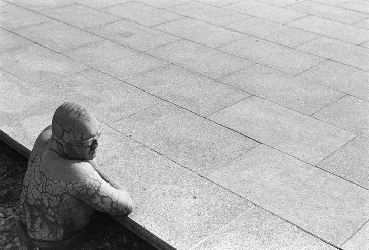 A statue of a man with cracked skin is partially submerged in water next to a tiled surface.