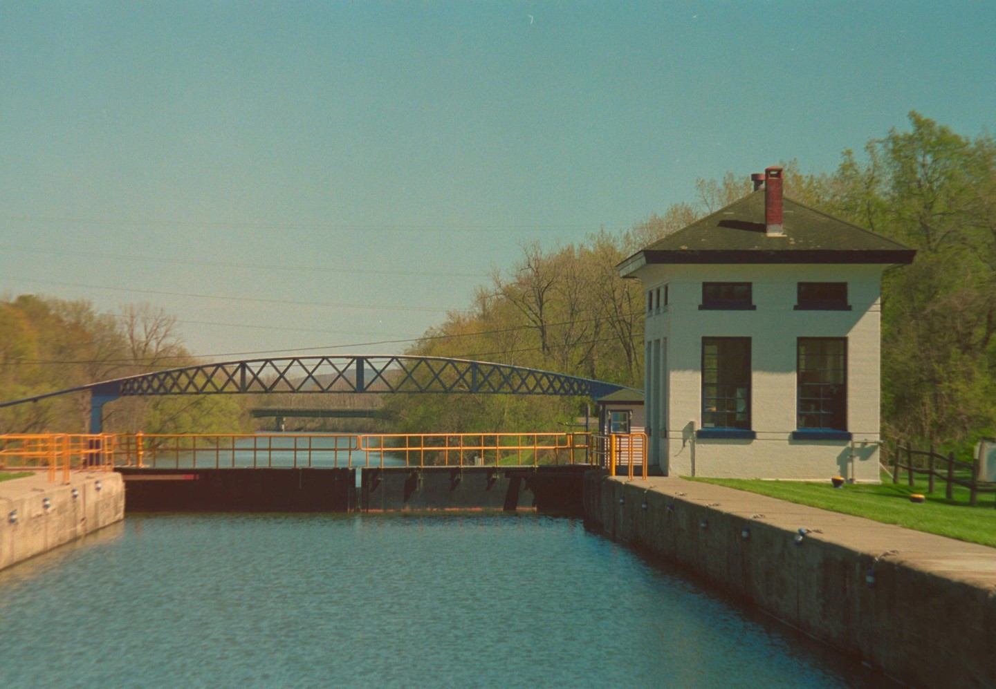A white building with a dark roof stands next to a canal with a bridge crossing it.