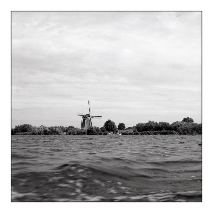 A windmill stands on the far bank of a body of water, with a small boat docked nearby.