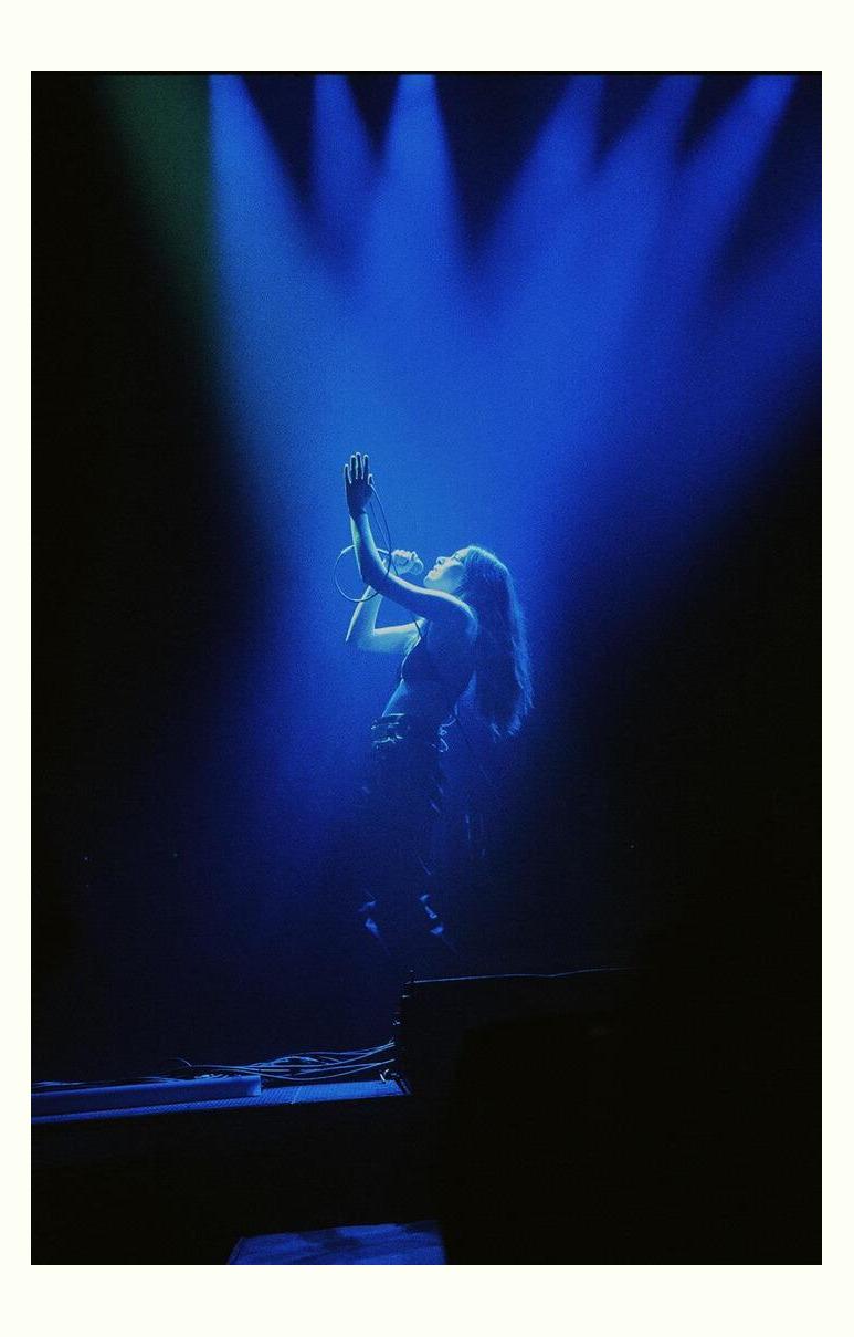 A woman sings into a microphone on a stage lit by blue spotlights.