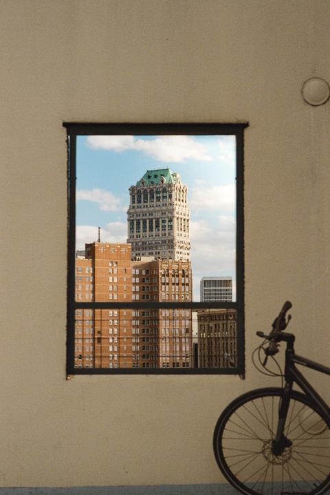 A tall building with a green roof is visible through a window, with a bicycle parked to the right.