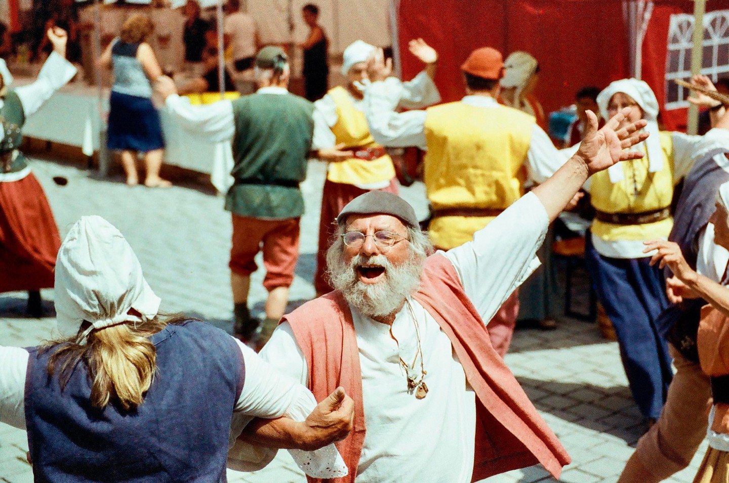 A group of people in period costumes dance in a circle on a paved surface.