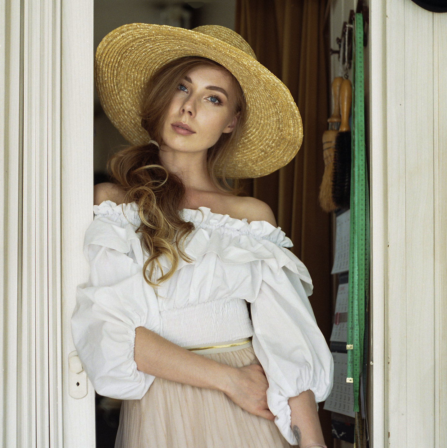 A woman wearing a straw hat and a white blouse stands in a doorway.
