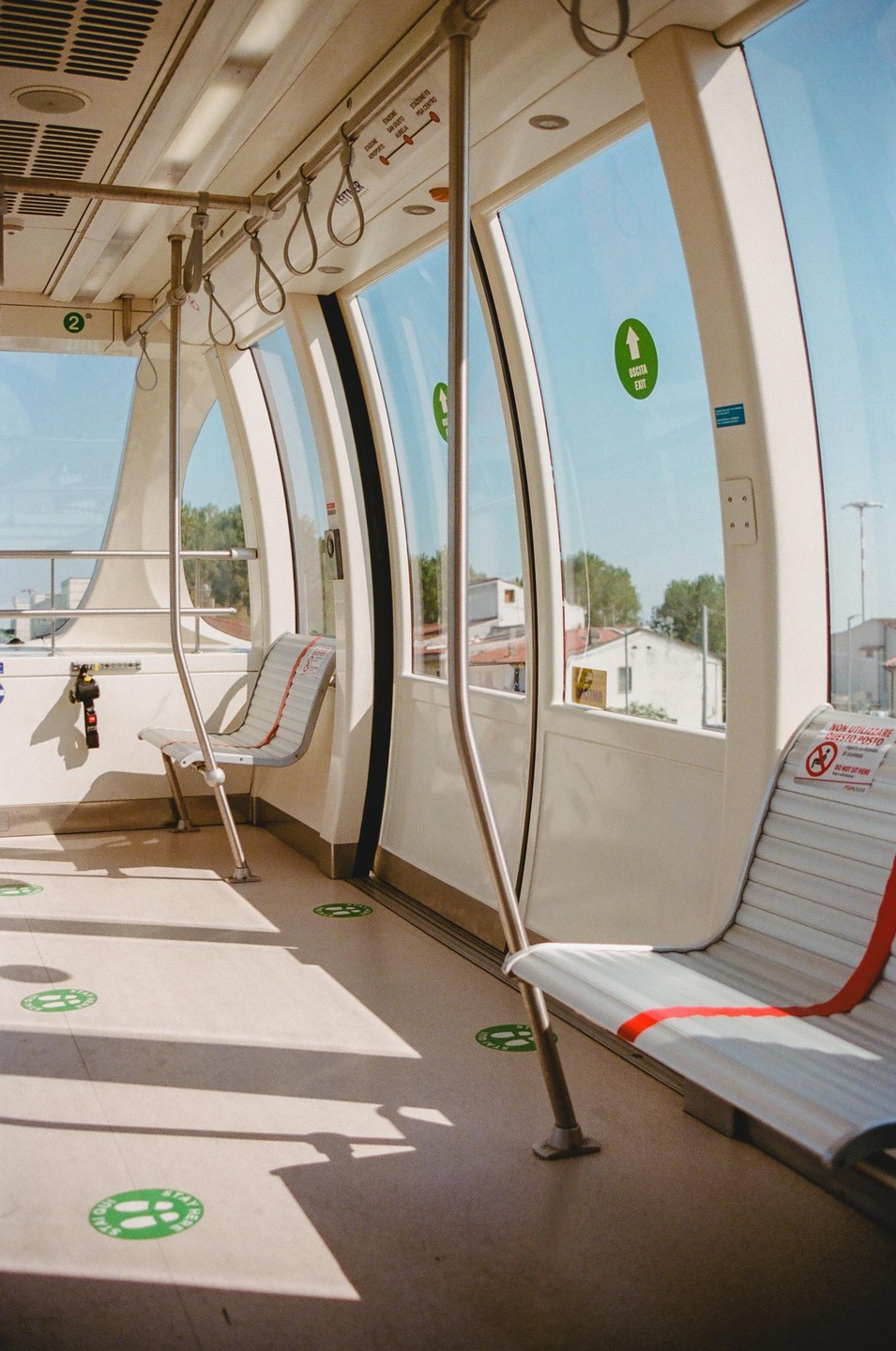 The interior of a modern, empty train car with large windows shows sunlight casting shadows on the floor.