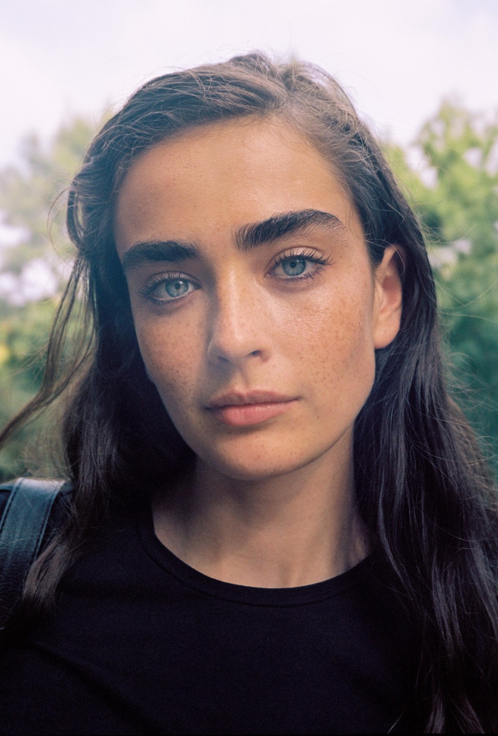A woman with long dark hair and blue eyes looks directly at the viewer.