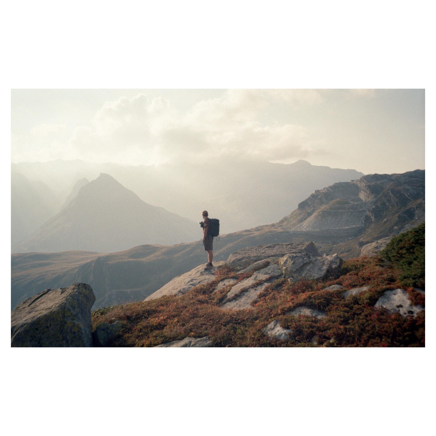 A man with a backpack stands on a rocky mountain overlooking a valley.