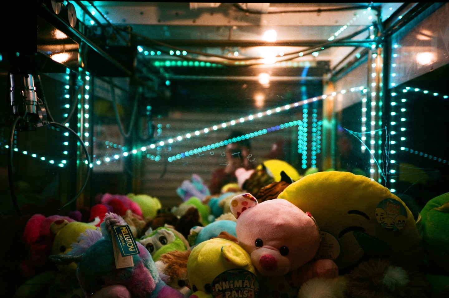 A claw machine filled with various plush toys is illuminated by colorful lights.
