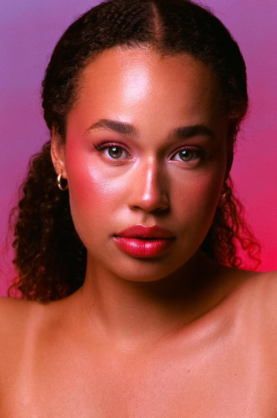 A woman with curly hair and bright makeup looks directly at the viewer.