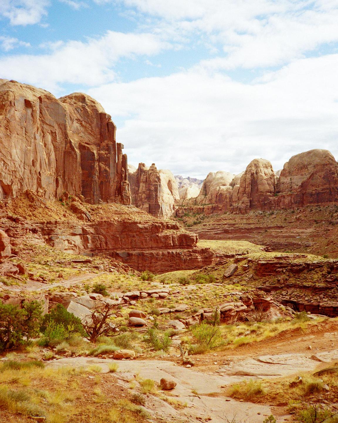 A vast desert landscape features towering red rock formations under a partly cloudy sky.