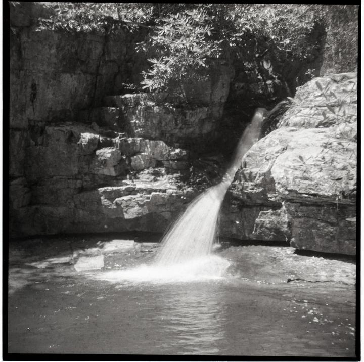 A waterfall cascades into a pool of water surrounded by rocky cliffs and foliage.