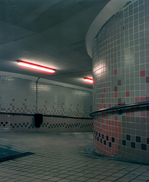 A tiled underpass is illuminated by red neon lights.