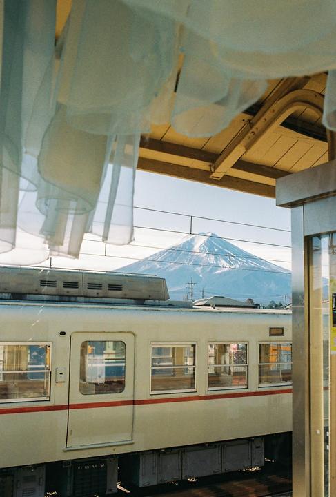 A train is parked at a station with a snow-capped mountain in the background, viewed through sheer curtains.