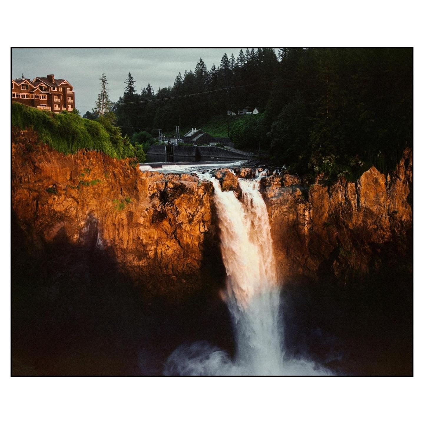 A waterfall cascades down a cliff face with a building visible on the cliff top.