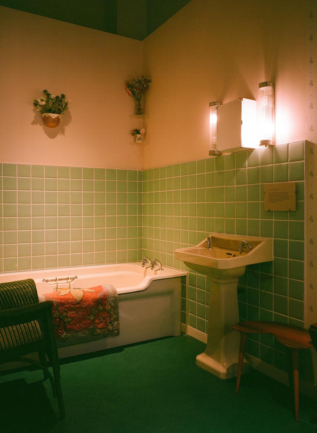 A vintage bathroom features green tiled walls, a white bathtub, and a pedestal sink.