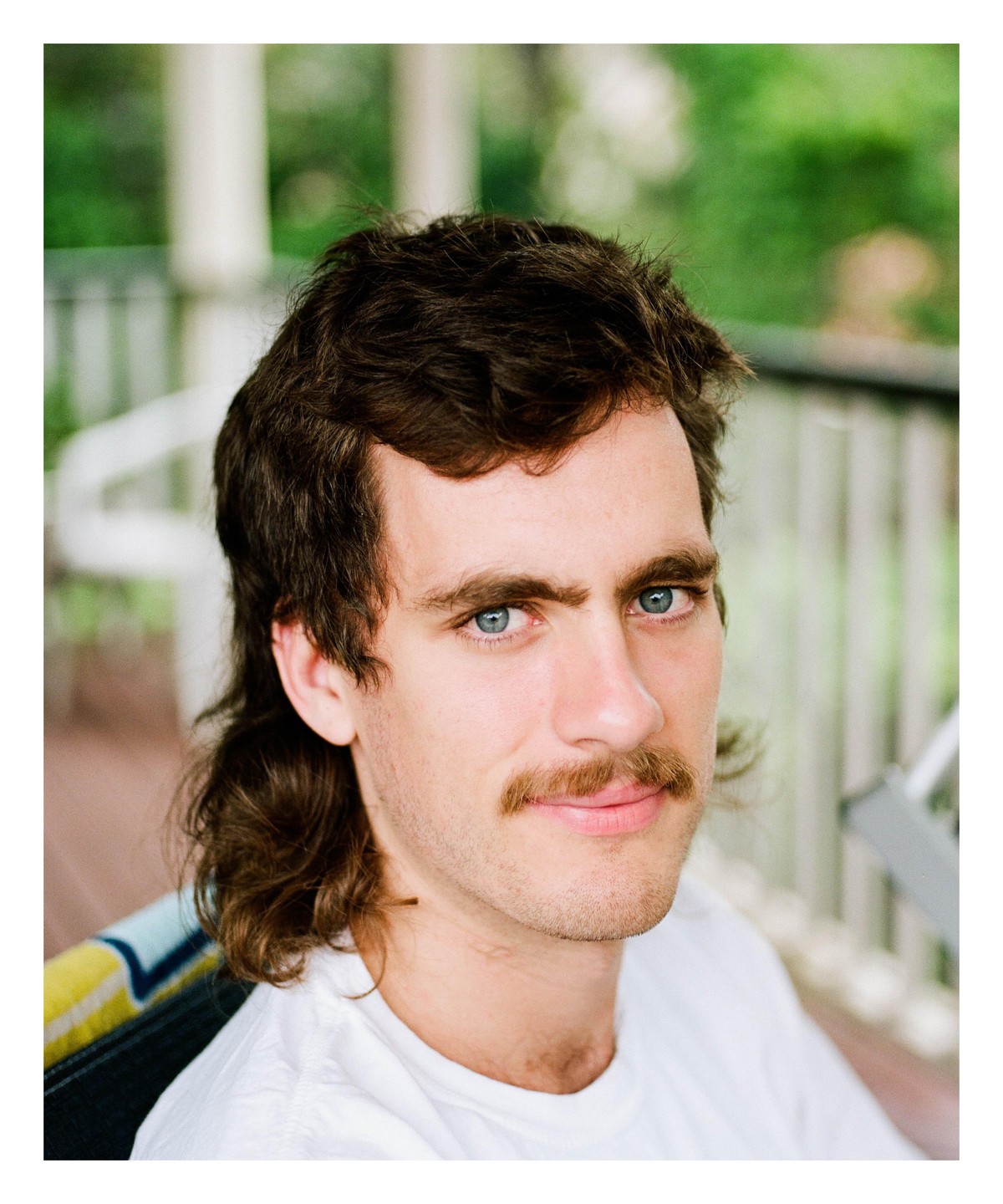 A man with a mullet and mustache looks directly at the viewer.