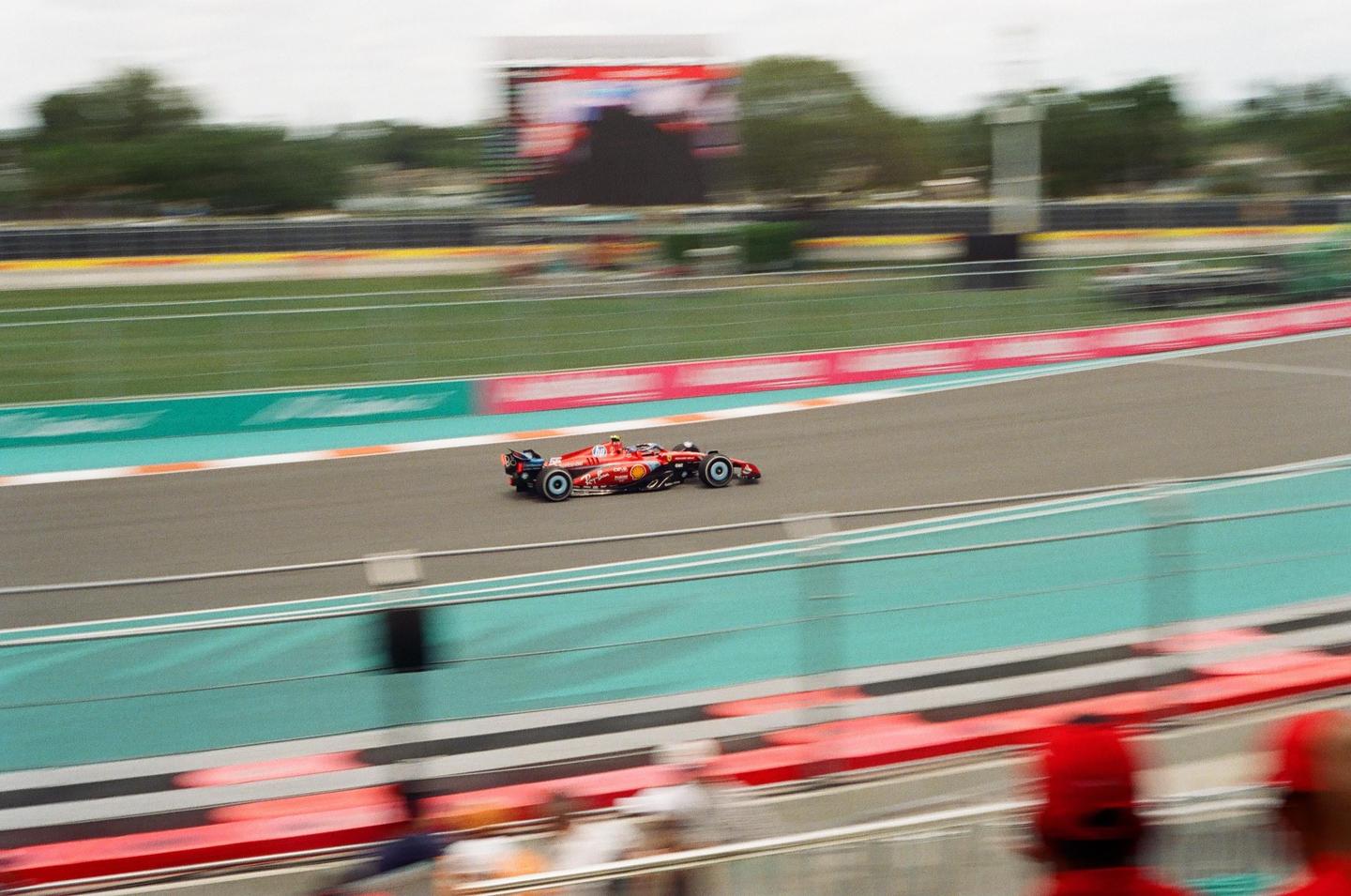 A red race car speeds around a track with blurred spectators in the foreground.